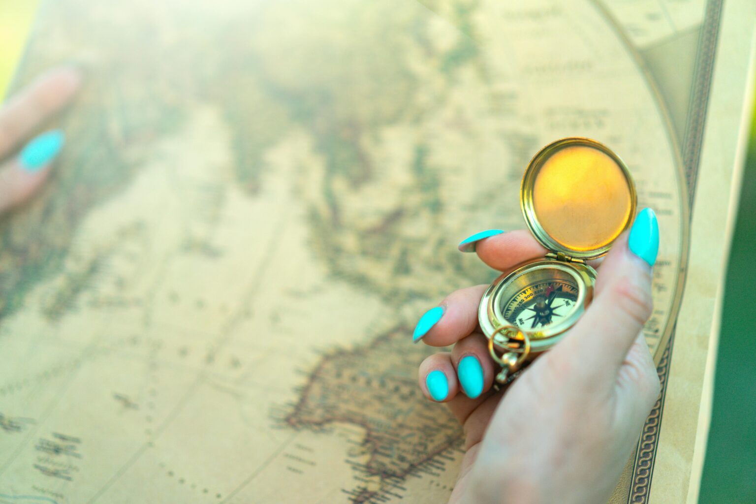 Close-up of a hand holding a vintage compass over an ancient map, symbolizing exploration and travel.