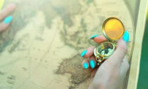 Close-up of a hand holding a vintage compass over an ancient map, symbolizing exploration and travel.